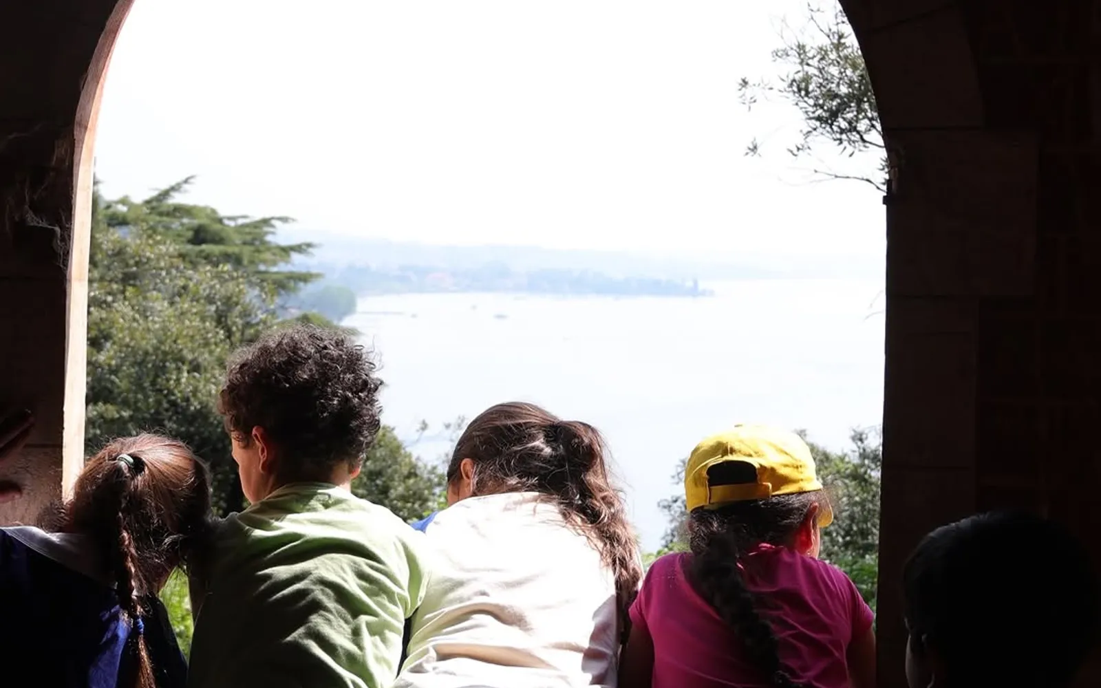 Un gruppo di visitatori sotto l’arco di pietra, con il lago di Garda sullo sfondo